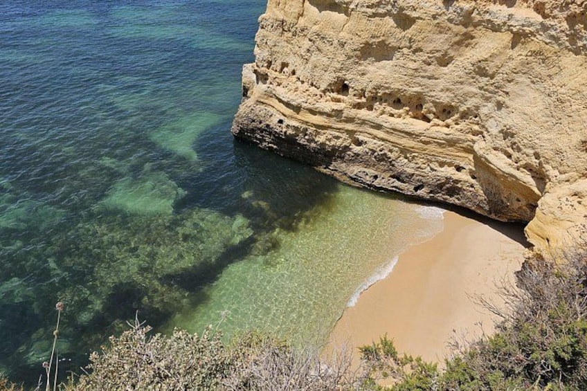 A coastal landscape with clear water, a sandy beach, and rocky cliffs. 4