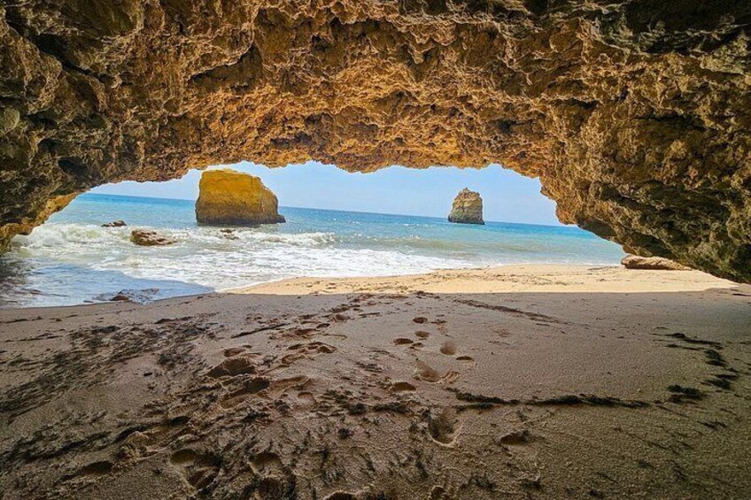 A beach with a large rock formation through a cave entrance, sandy beach, and ocean waves. 5