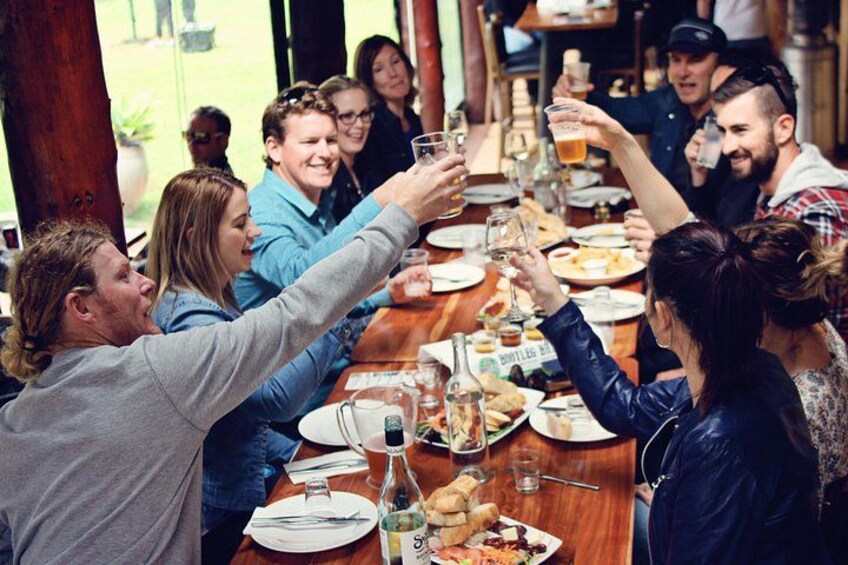 Un groupe de personnes trinquant autour d’une table en bois, devant une variété de plats et de boissons. 3