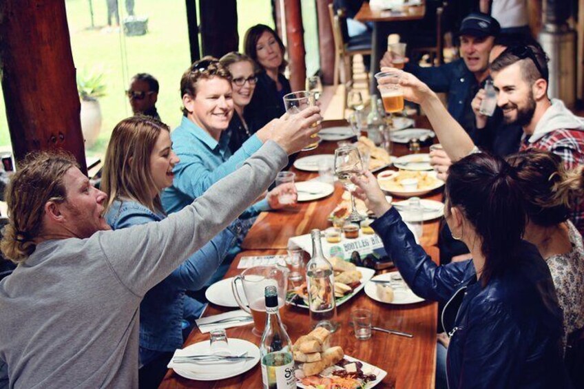 A group of people toasting at a wooden table with various dishes and drinks. 3