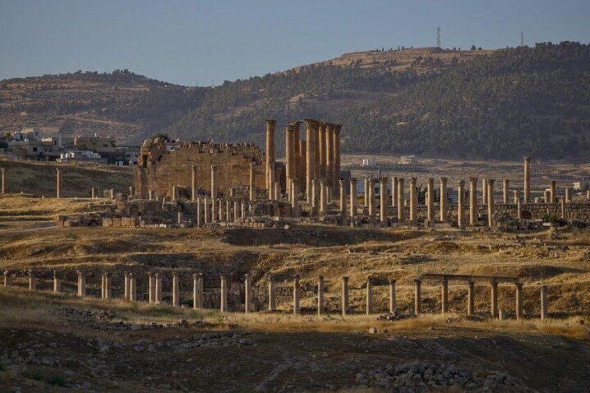 Ancient ruins with columns and a large stone structure, set against a hilly backdrop. 2