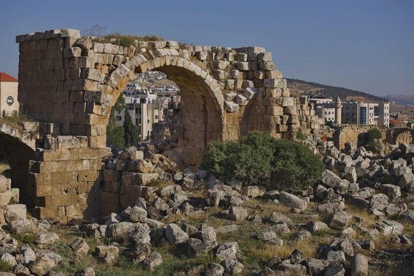 Ancient stone ruins with arches, scattered rocks, and a distant cityscape. 3