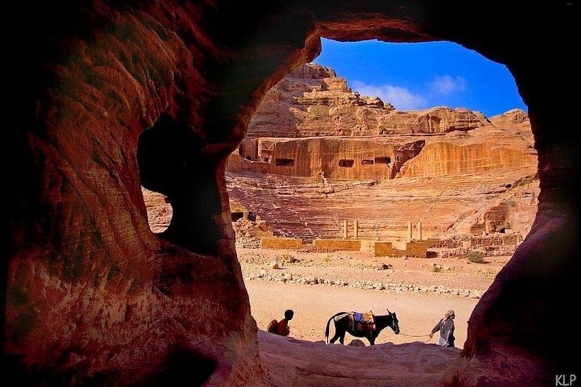 Formación rocosa con una abertura de cueva, paisaje desértico y un camello. 5