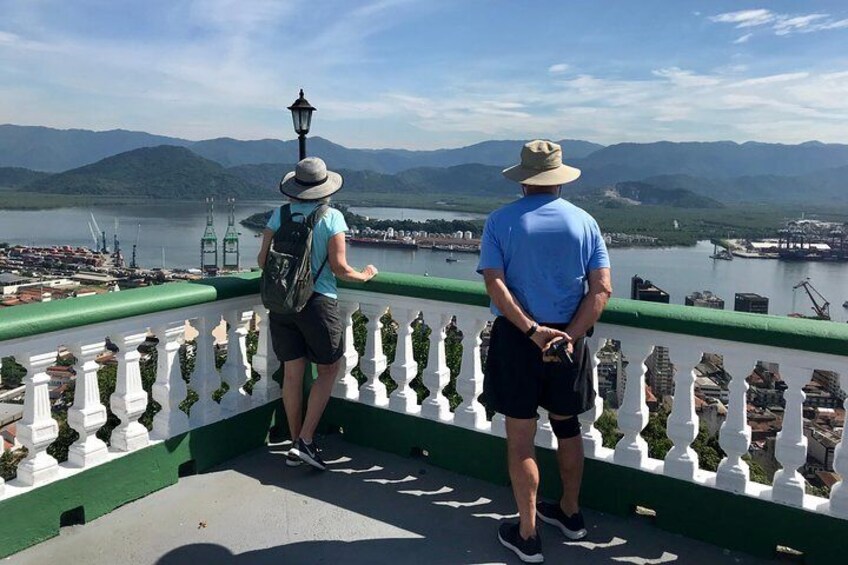 Two people standing on a green and white railing overlooking a body of water with mountains in the background. 2