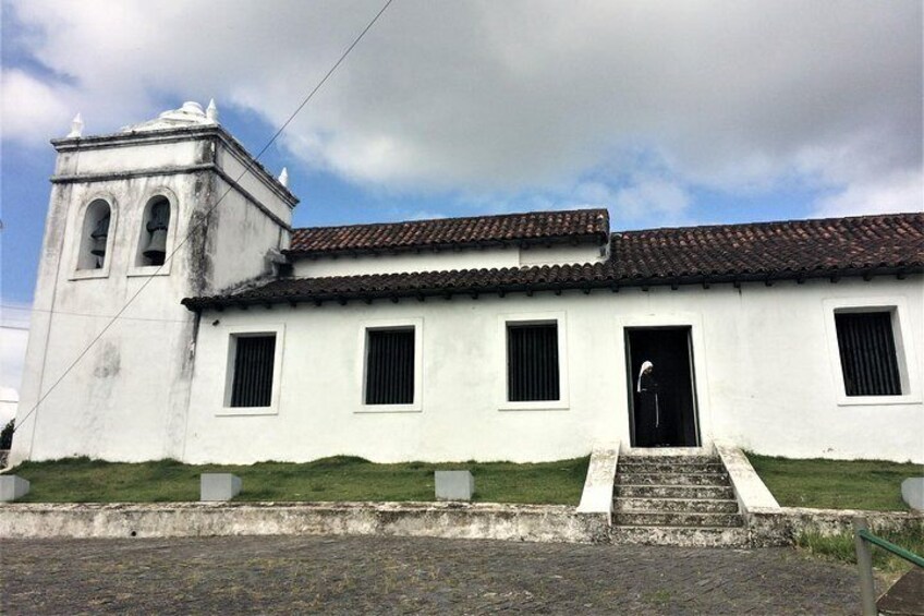 A white colonial-style building with a bell tower, a tiled roof, and a set of stairs leading to the entrance. 4