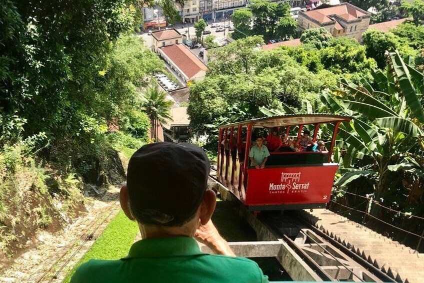 A red trolley with passengers, a man in a green shirt, and a lush green landscape with buildings in the background. 5