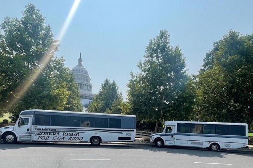 Two white tour buses parked in a lot with the U.S. Capitol building in the background. 2