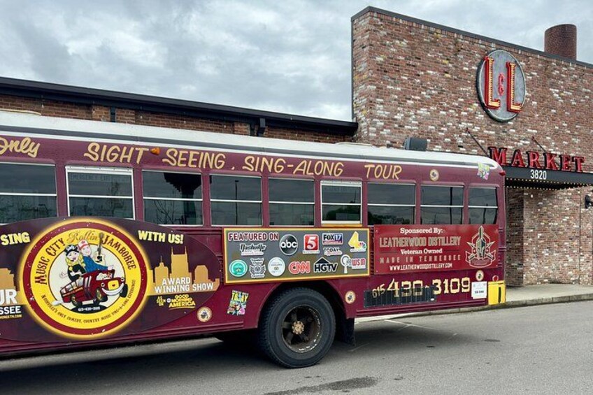A tour bus with advertisements and a brick building in the background. 4