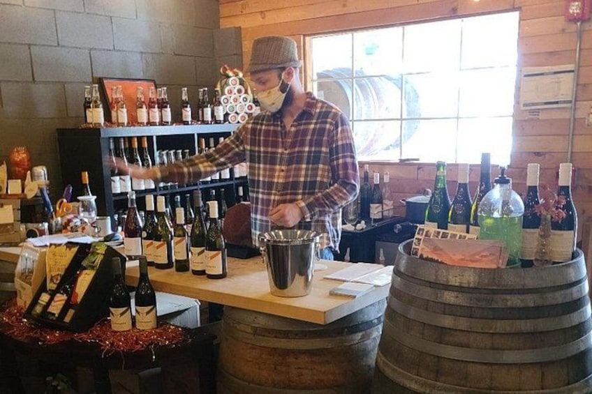 A person at a bar counter with wine bottles and a barrel. 2