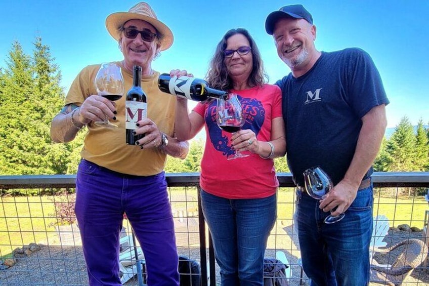 Three people holding wine bottles and glasses outdoors. 3