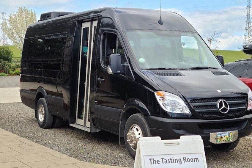 Een zwarte Mercedes bestelwagen geparkeerd op een grindpad, met een bord met daarop 'The Tasting Room'. 2