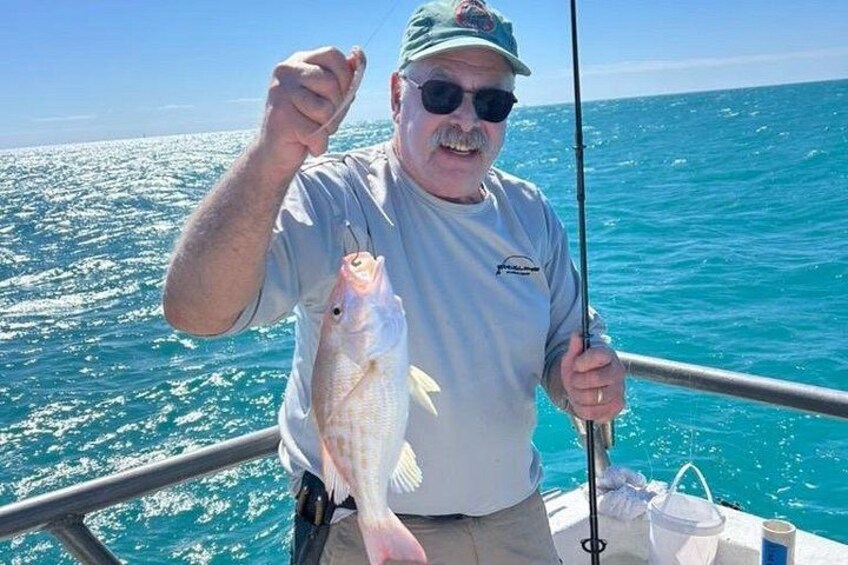 Eine Person hält einen Fisch in einem Boot, im Hintergrund das Meer. 5