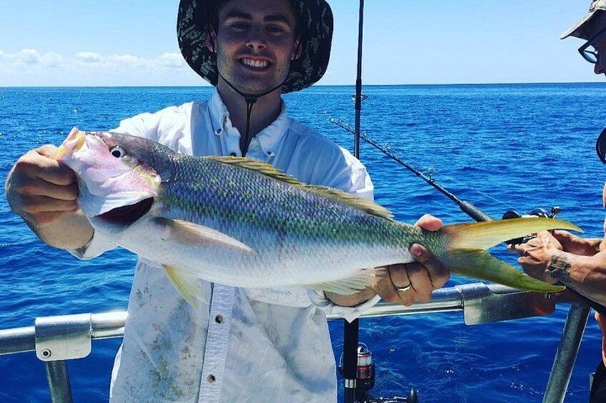 Eine Person hält einen großen Fisch auf einem Boot, im Hintergrund das Meer. 1