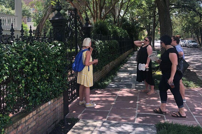 A sidewalk with a brick pattern, a metal fence, and green foliage. 2