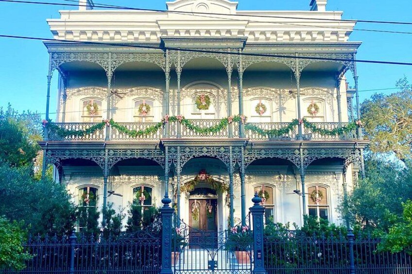 A large, ornate Victorian-style house with multiple balconies and a front porch, decorated with garlands. 4