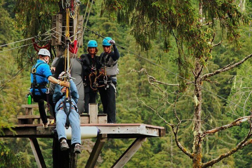 A group of people on a platform with ropes and harnesses, preparing for an activity in a forested area. 2
