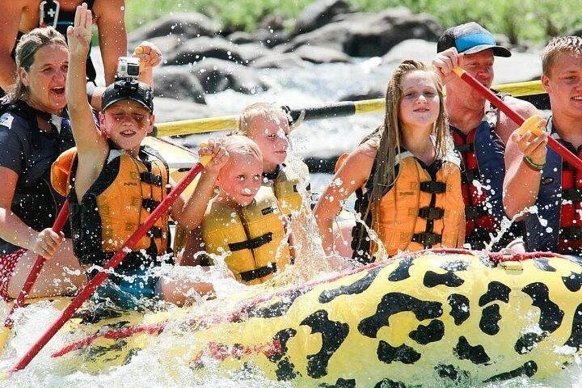 A group of people in a yellow raft with black spots, wearing life jackets, navigating through water. 4