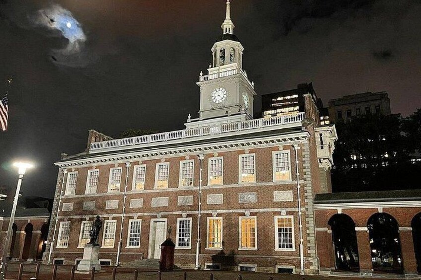 Un edificio histórico con una torre de reloj, ventanas iluminadas y una bandera estadounidense. 3