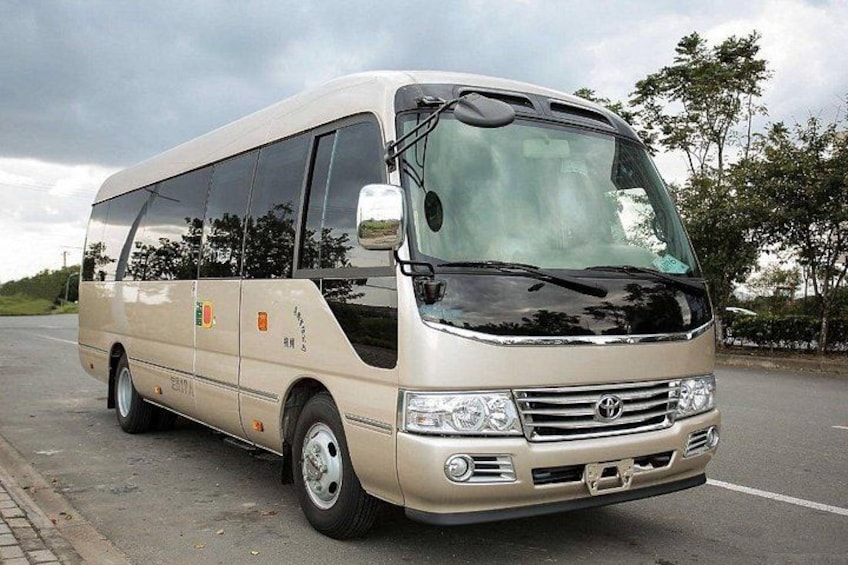 A beige bus with a black front grille, side mirrors, and a license plate. 2