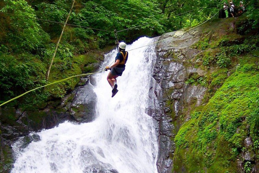 A person zip-lining over a waterfall in a forested area. 3
