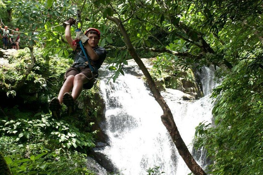 A person rappelling down a waterfall surrounded by lush greenery. 4