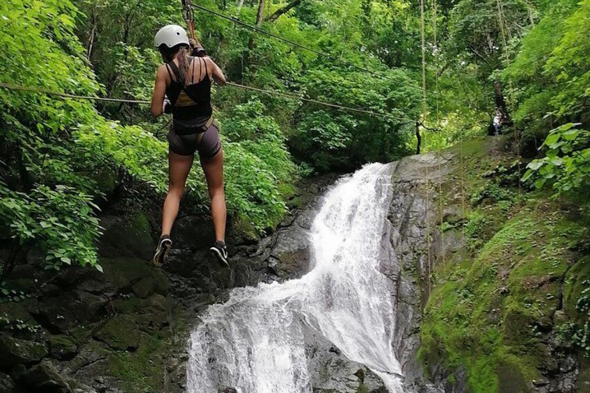A person zip-lining over a waterfall in a forested area. 2