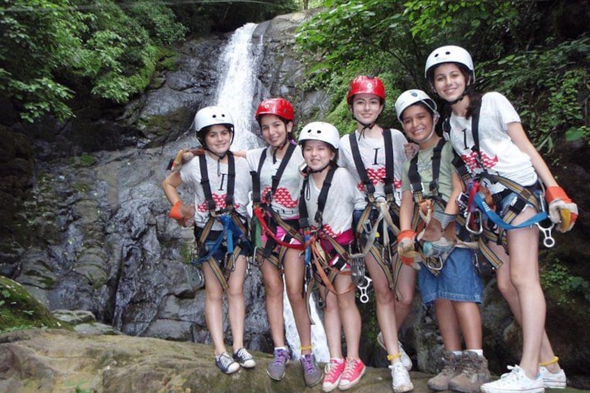 A group of people with helmets and harnesses in front of a waterfall. 3
