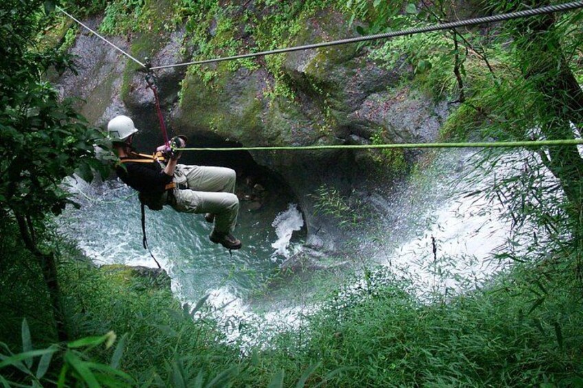A person rappelling down a rocky cliff into a river surrounded by dense greenery. 2
