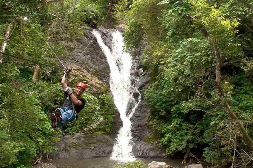 A person rappelling down a waterfall surrounded by dense forest. 5
