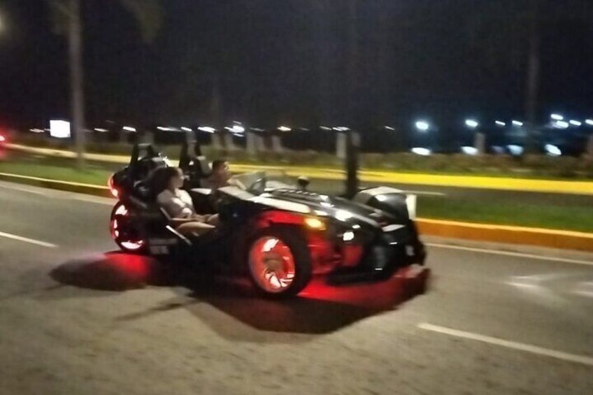 Un véhicule doté d’une grande roue arrière et d’une petite roue avant, vraisemblablement un jouet ou un véhicule original, circule sur une route la nuit. 3