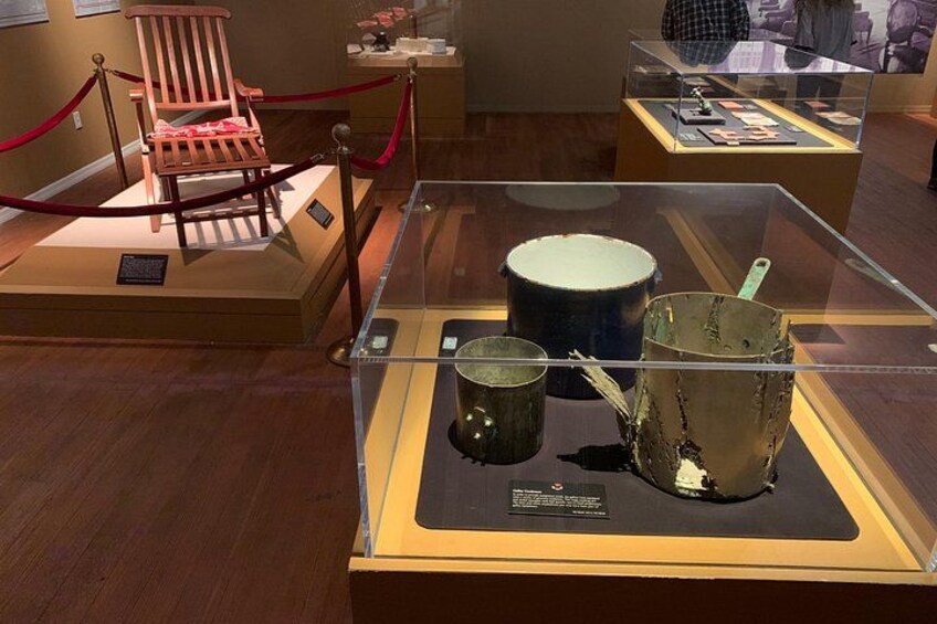 A museum exhibit with a wooden chair, a glass display case containing three metal objects, and a red rope barrier. 3