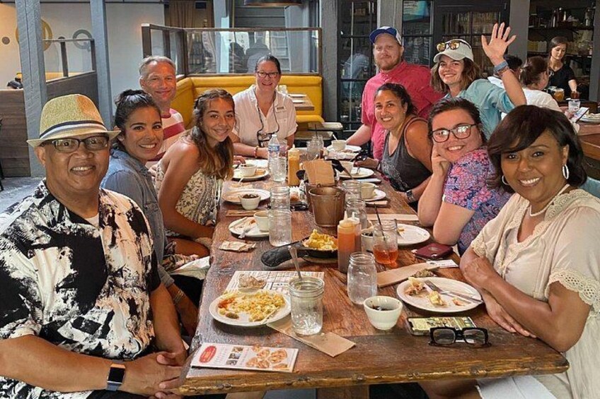 A group of people sitting around a wooden table in a restaurant, with various dishes and drinks on the table. 2