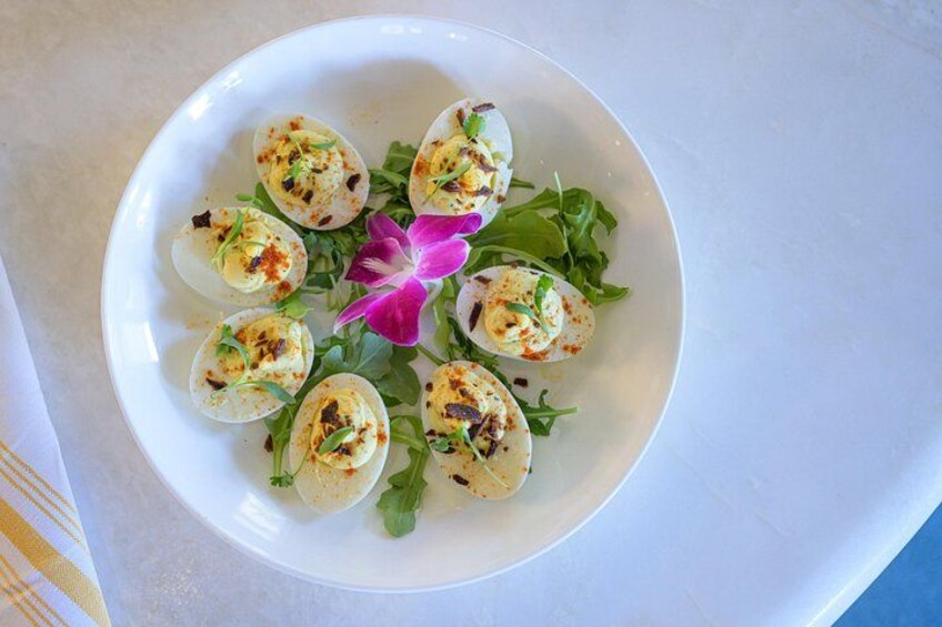 A plate of deviled eggs garnished with herbs and a purple flower. 5