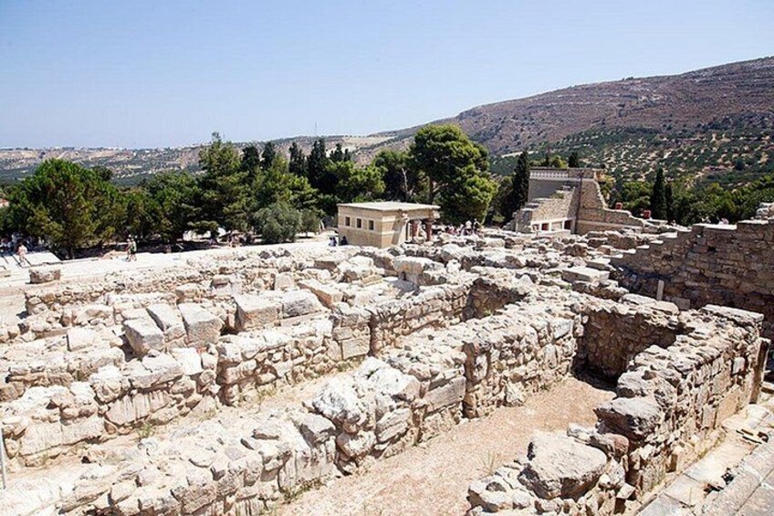 Ancient ruins with stone blocks, a building in the background, and a hilly landscape. 2