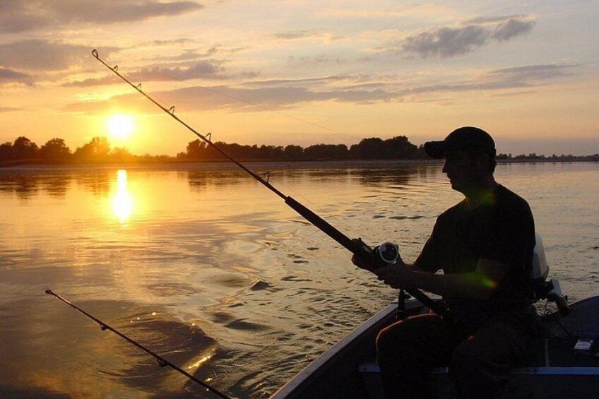 Una persona pescando al atardecer junto a un cuerpo de agua tranquilo. 4