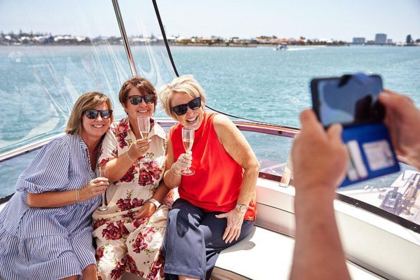 Trois personnes se trouvent sur un bateau, l’une d’entre elles prend une photo. On aperçoit une étendue d’eau et une côte lointaine en arrière-plan. 4