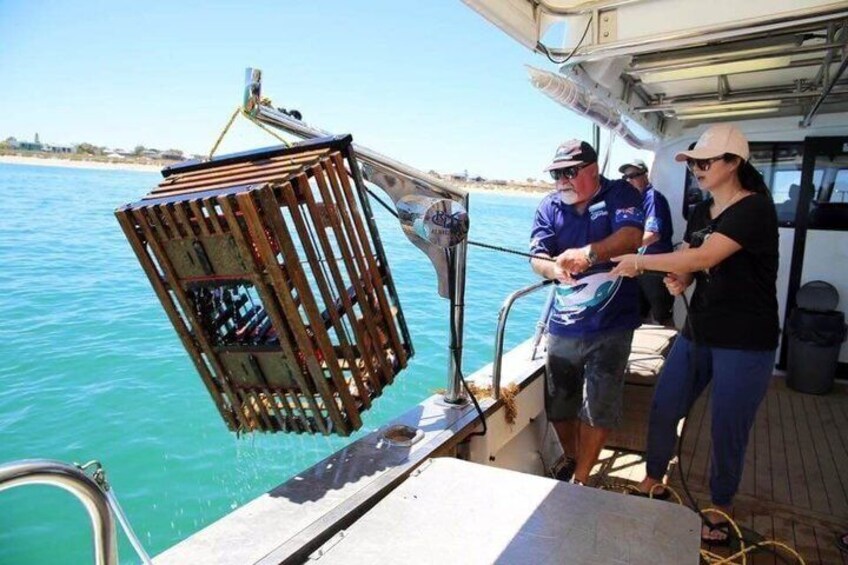 A boat with a wooden crate on the deck, a person operating a winch, and calm water in the background. 2