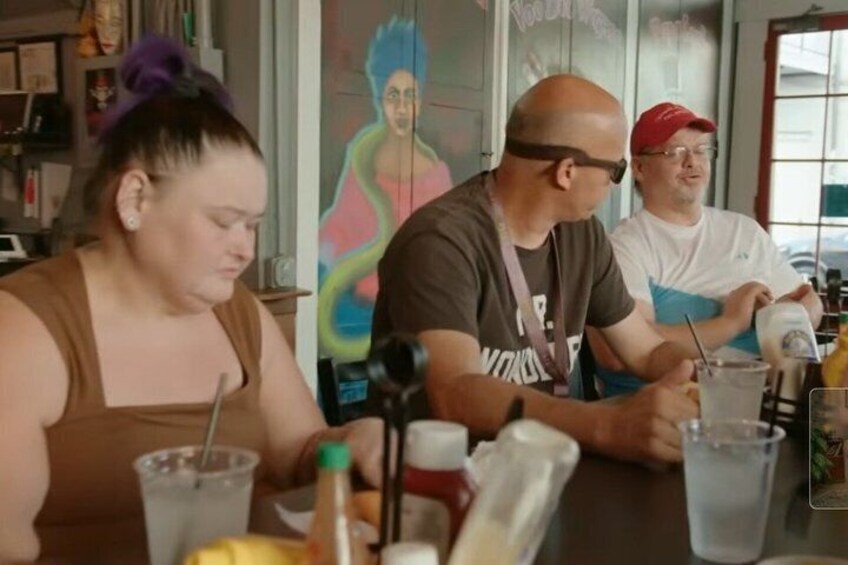 Trois personnes sont assises à une table, devant des boissons, une bouteille et une tasse. 2