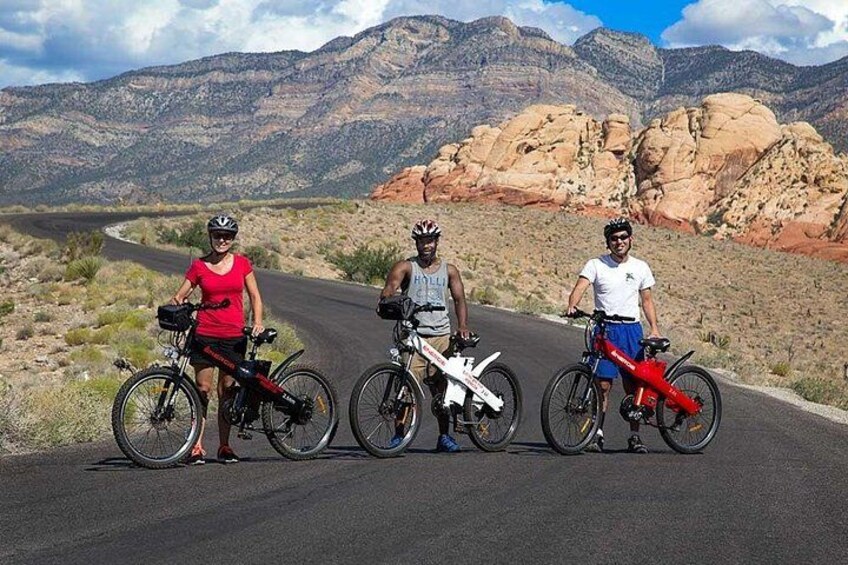 Trois cyclistes sur une route asphaltée, avec un paysage montagneux en arrière-plan. 3