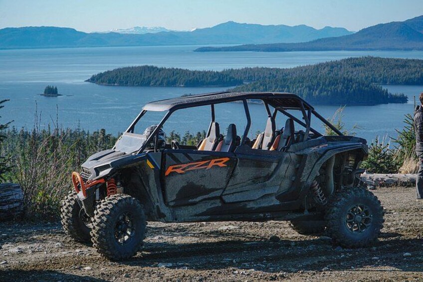 A Polaris RZR off-road vehicle parked on a dirt path with a lake and mountains in the background. 2
