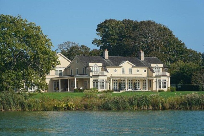 Una casa grande junto a un lago, con césped cuidado y árboles. 3