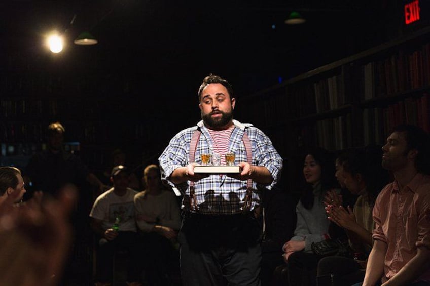 A person holding a tray with drinks in a dimly lit indoor setting with bookshelves in the background. 2