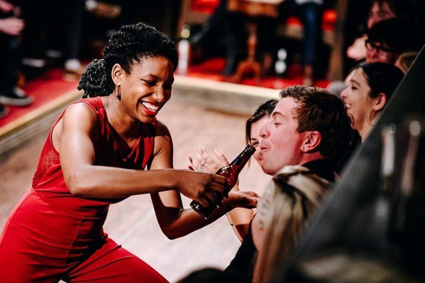 A person in a red dress holding a bottle, another person in a beige jacket, and a blurred background with people. 4