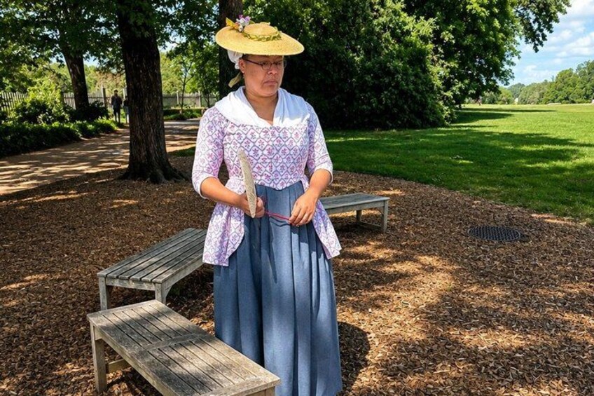 A person in historical attire standing in a park with benches and trees. 5