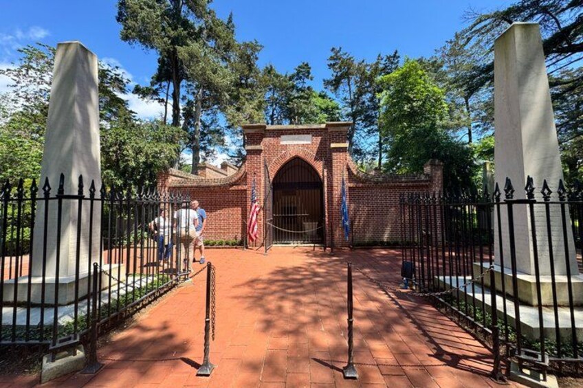 A brick entrance gate with an American flag, surrounded by a metal fence and trees. 2