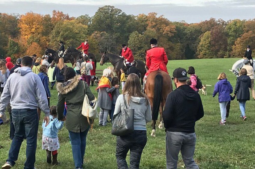A group of people gathered in a grassy field with horses and riders. 3