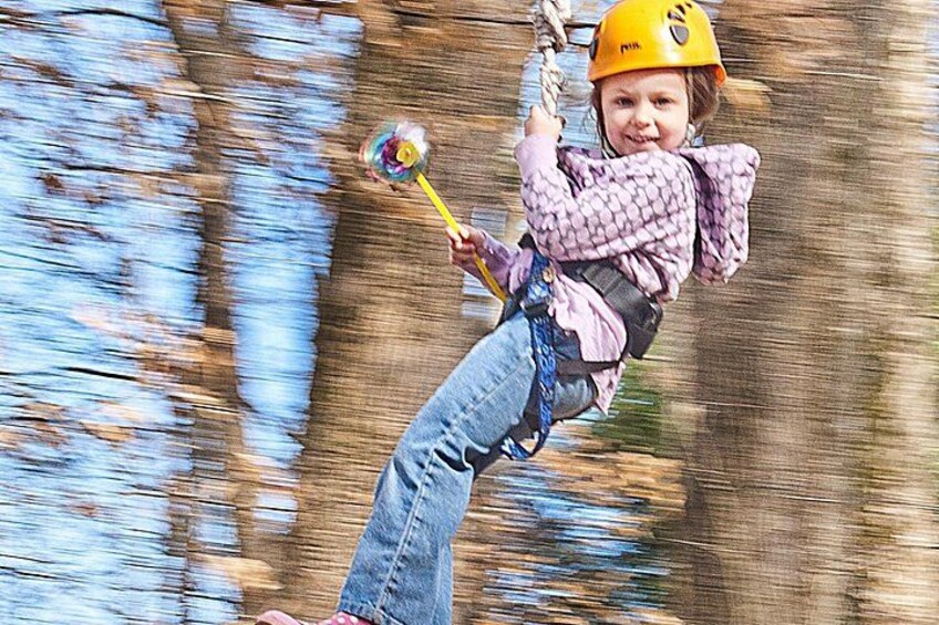 A child on a zip line, wearing a helmet and harness, with trees in the background. 3