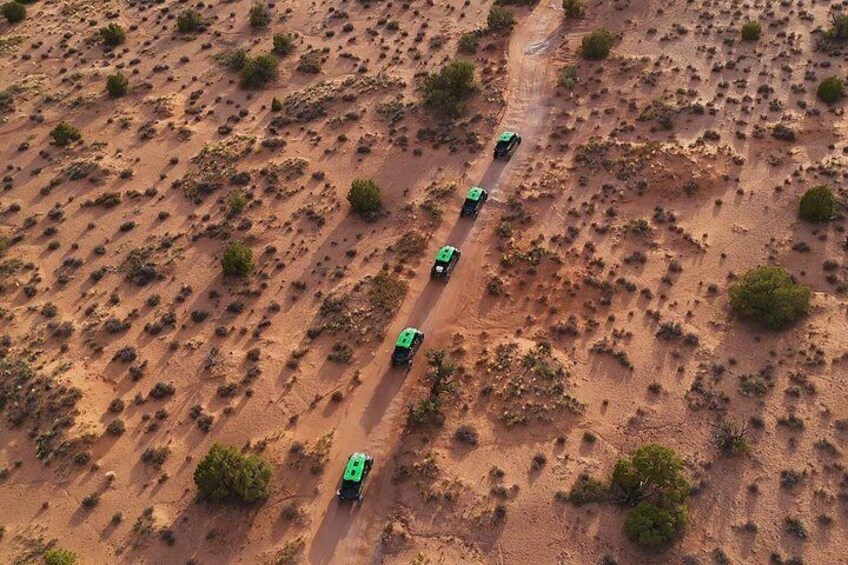 A desert landscape with a dirt road and four green vehicles. 3