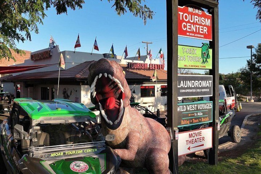 A dinosaur statue, a green car, and a sign for the Moab Tourism Center. 2