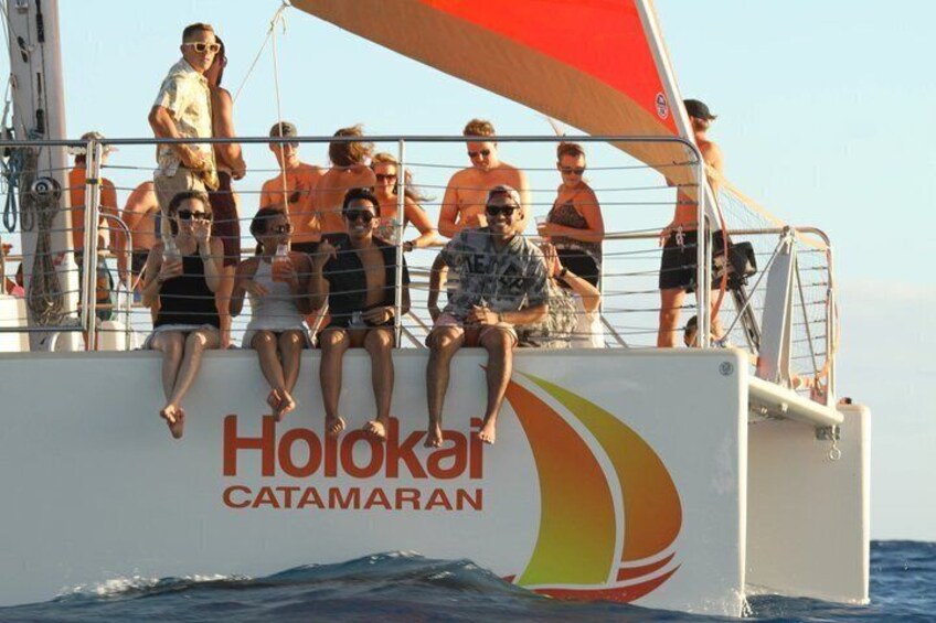 A sailboat with the name 'Hoioka Catamaran' on its side, people sitting on the deck, and the ocean in the background. 2